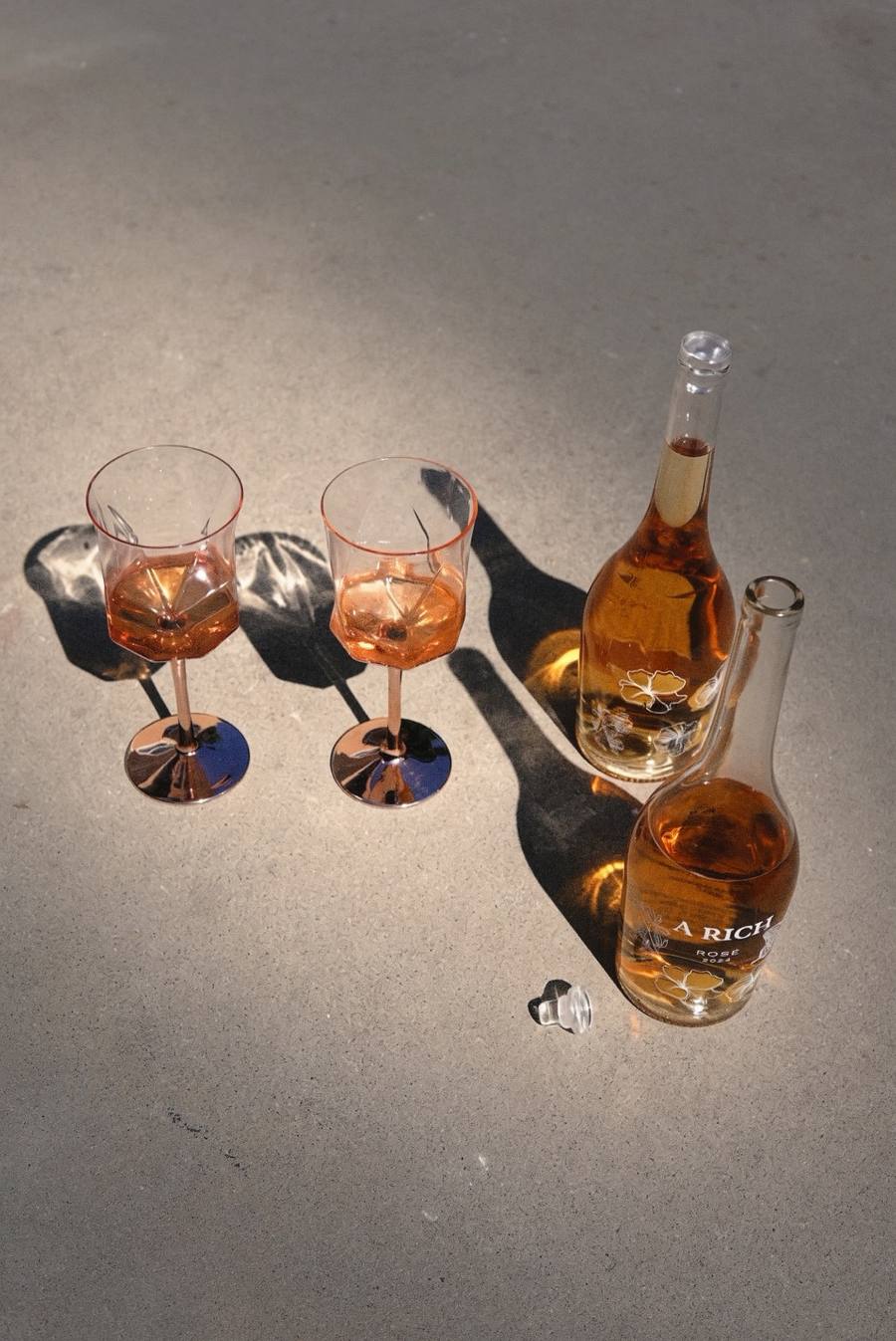 Two glasses of A Rich Rosé and bottles casting long shadows in the sun